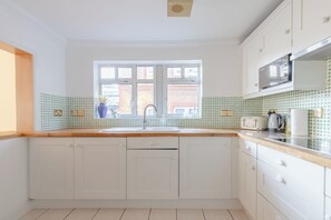 Een keuken met witte kastjes, een dubbele spoelbak en een raam met uitzicht op een bakstenen gebouw.
