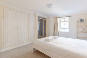 A bedroom with a bed, a wardrobe, a window, and a shelf with items.