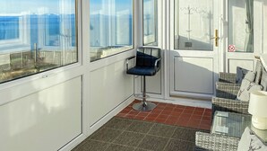 Ein Zimmer mit großen Fenstern, einem Sessel, einem kleinen Tisch und einer Couch.