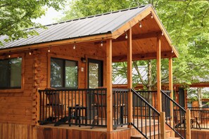 A wooden cabin with a porch, large windows, and a staircase leading to the entrance.