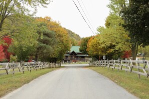A road leading to a lodge with a green roof, surrounded by trees with autumn foliage.