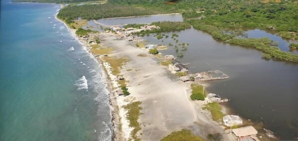 An aerial view of a coastal area with a beach, a small settlement, and a large body of water. - Urantia Beach Hostel & Camping (San Onofre)