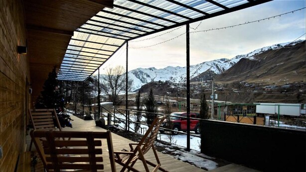 Une terrasse en bois, protégée par une paroi de verre, qui offre une vue sur un paysage montagneux enneigé.