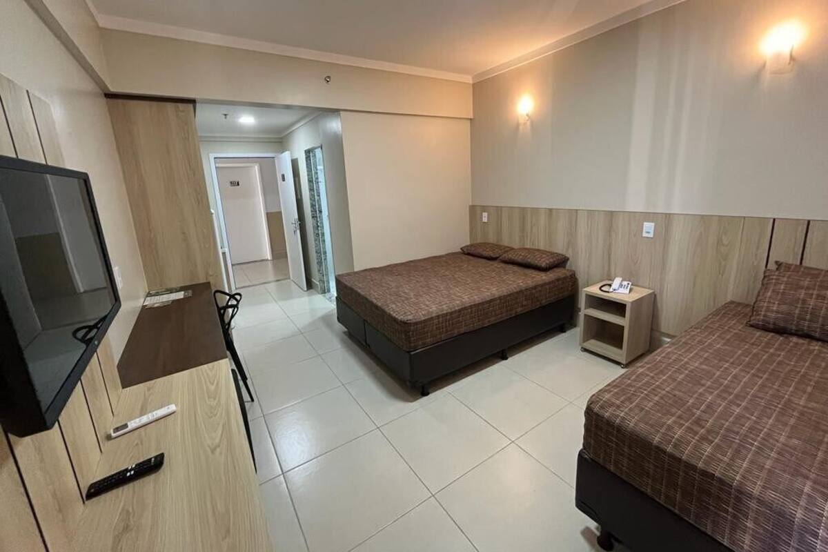 A hotel room with two beds, a TV, a bedside table, and a door leading to another room.