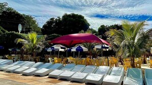 A poolside area with lounge chairs and umbrellas, surrounded by palm trees and a clear sky. - Spazzio diRoma Com Parque Acqua Splash (Caldas Novas)