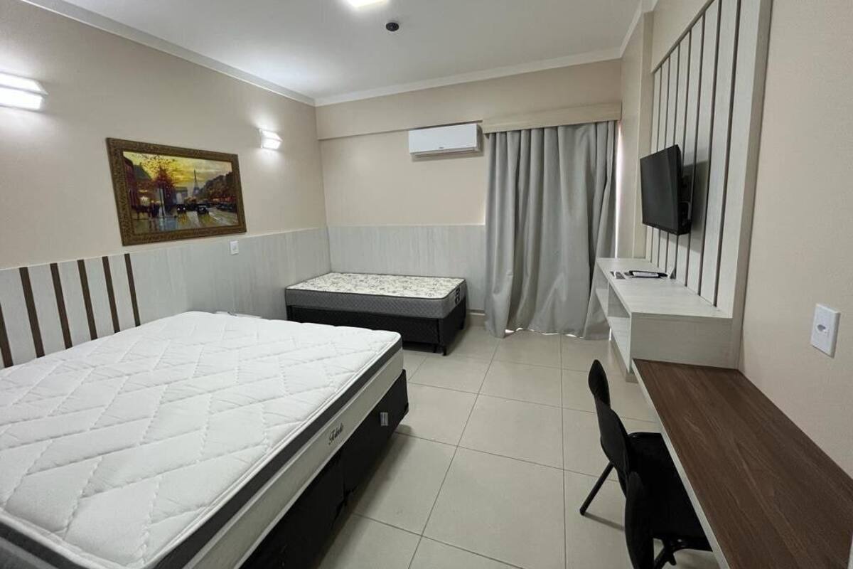 A hotel room with a bed, a desk, a chair, a television, and a painting on the wall.
