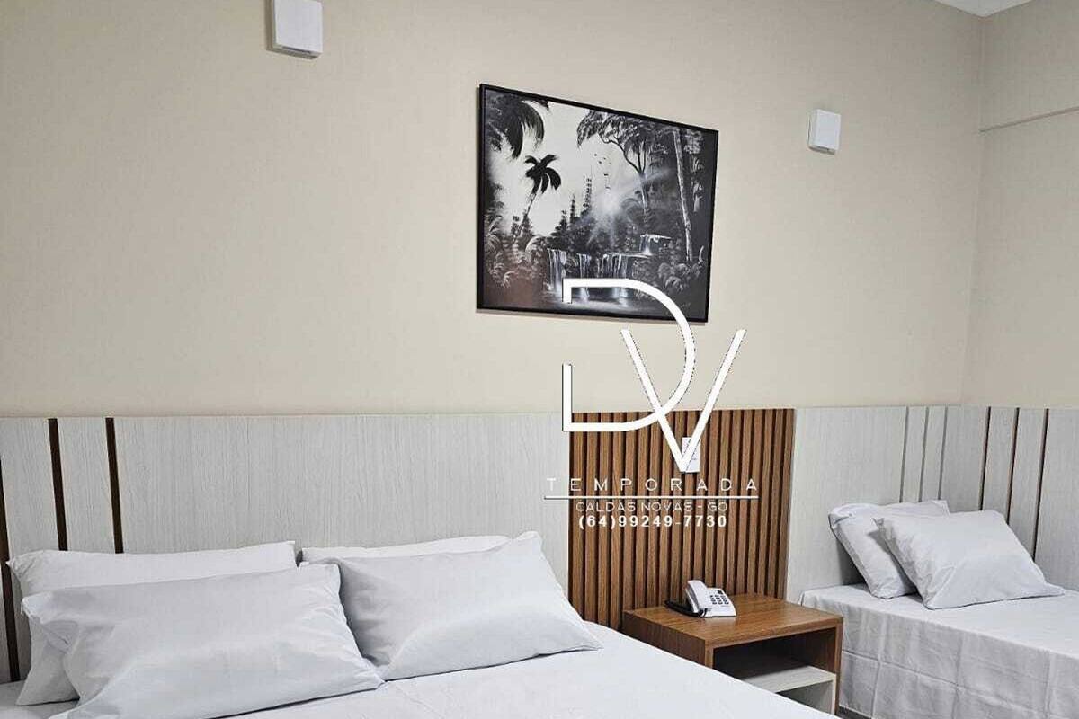 A hotel room with a large bed, two smaller beds, a wooden nightstand with a phone, and a wall-mounted poster.