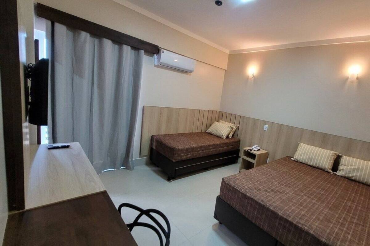 A hotel room with two beds, a desk, a chair, a nightstand, and a window with curtains.