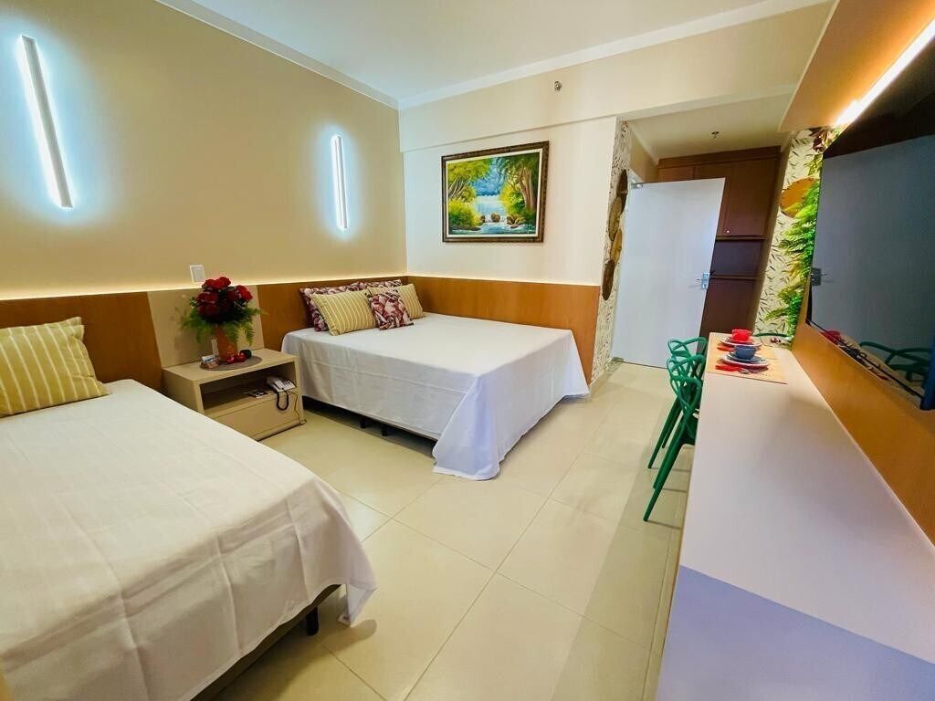 A hotel room with two beds, a desk with a chair, a painting on the wall, and a shower area.