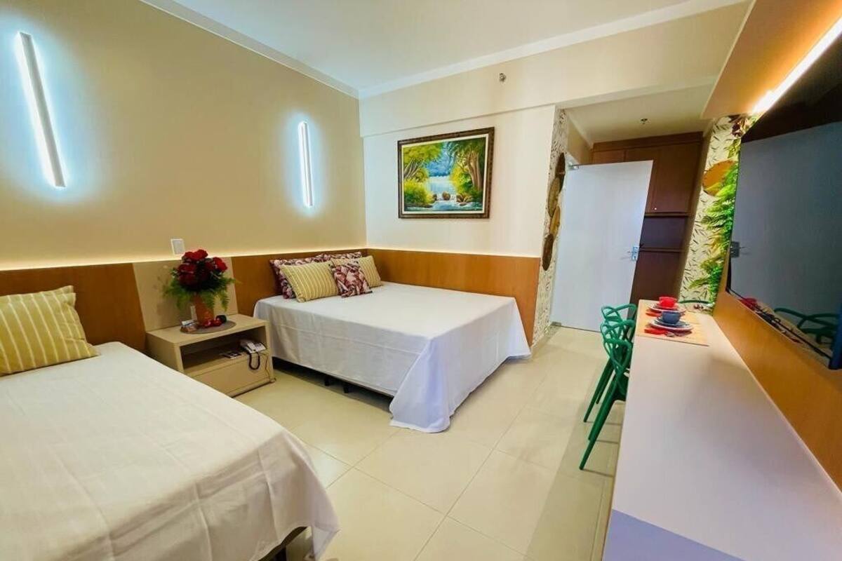 A hotel room with two beds, a desk with a chair, a painting on the wall, and a shower area.