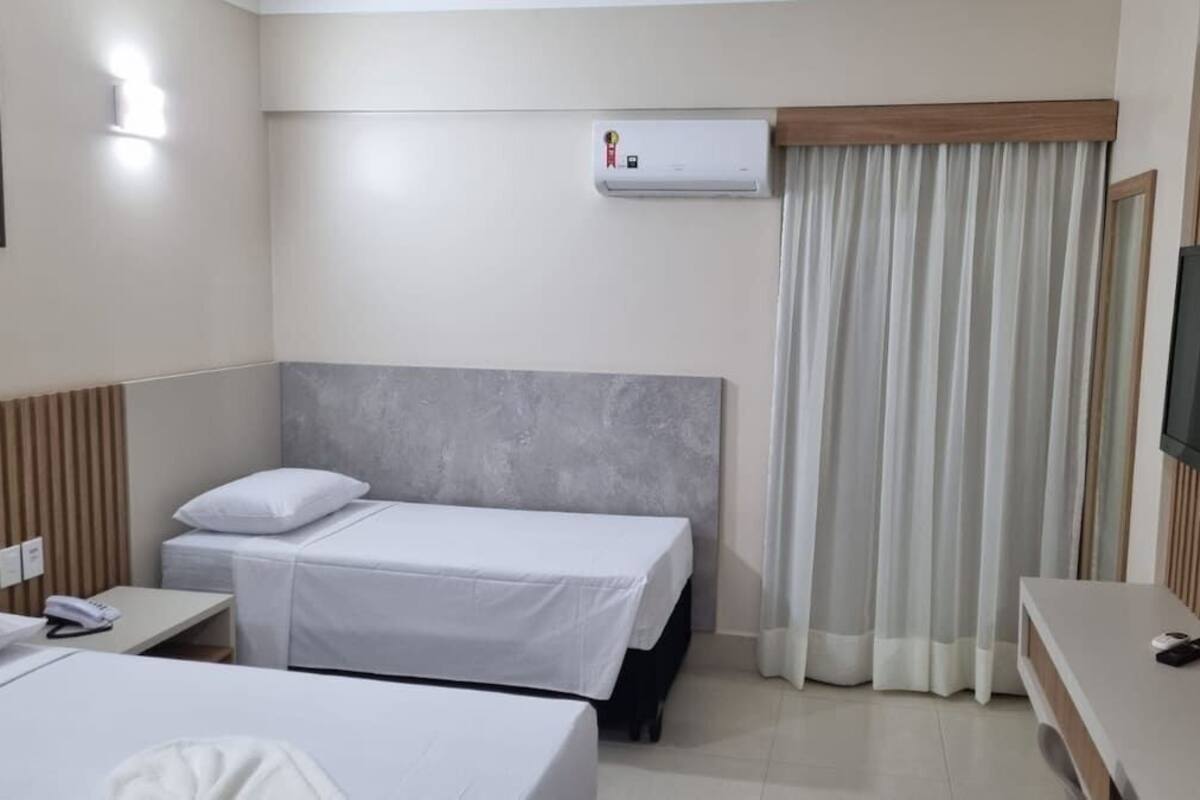 A hotel room with two beds, a TV, a desk, and a window with curtains.