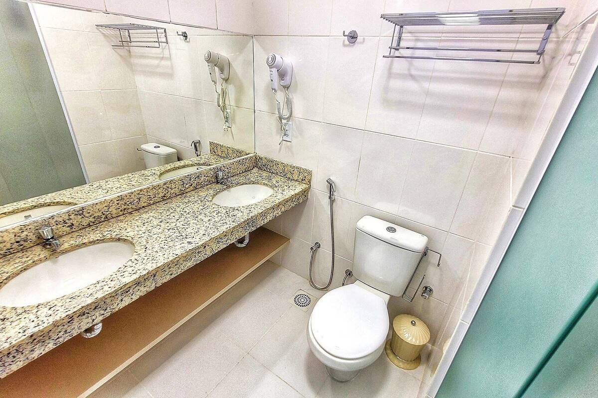 A bathroom with a granite countertop, two sinks, a toilet, and a shower.