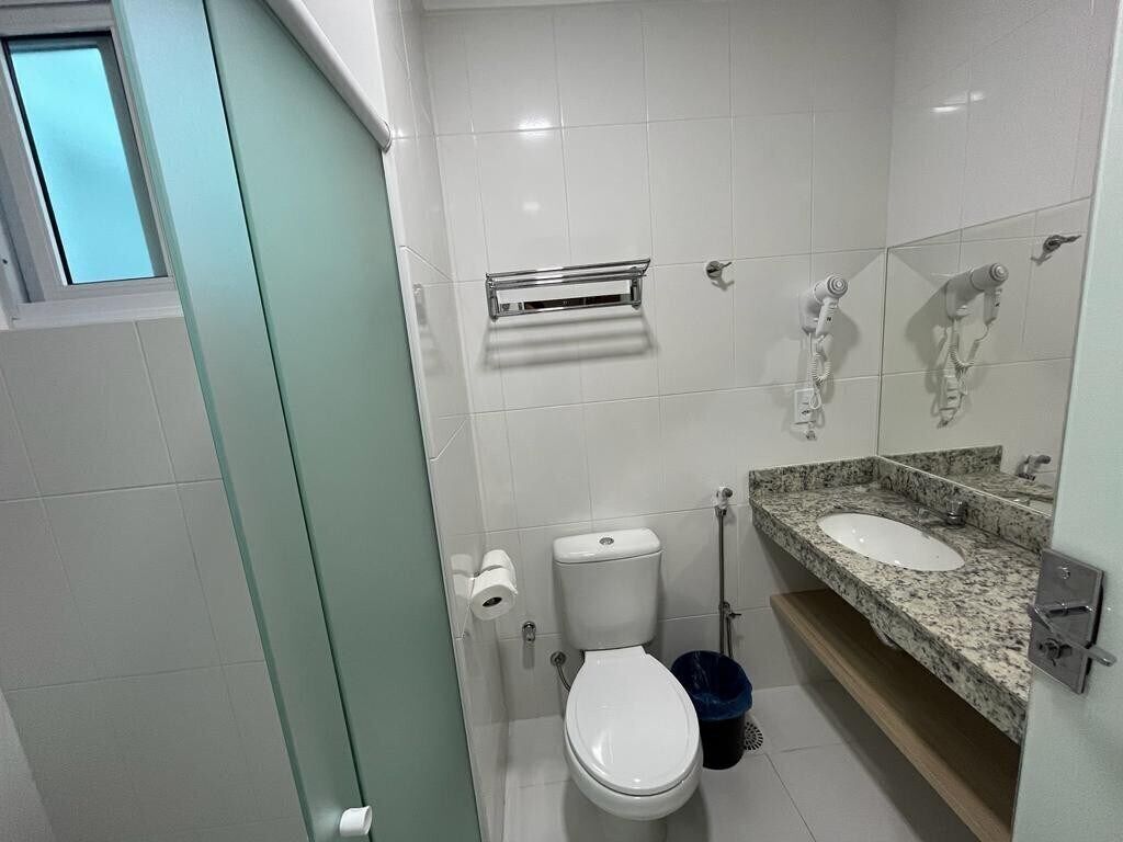 A bathroom with a toilet, a sink, a mirror, and a trash bin.