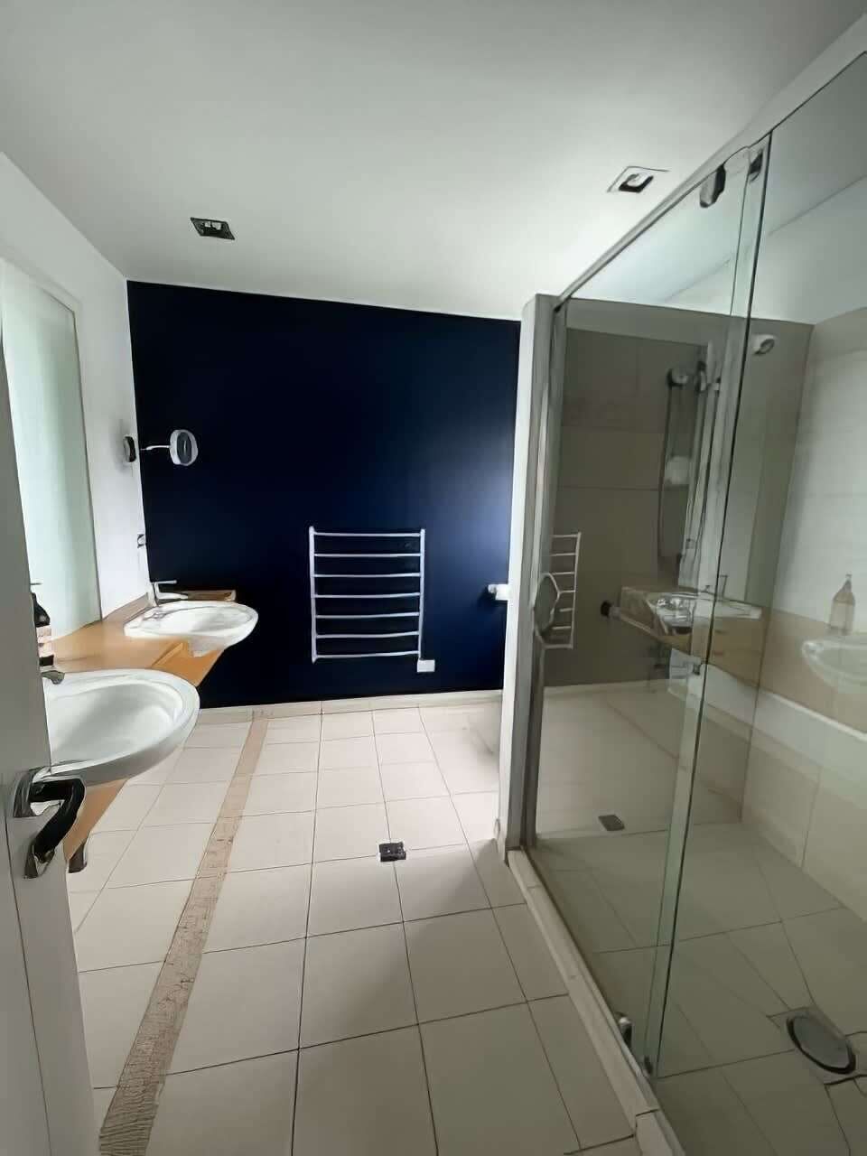 Un bagno moderno con box doccia in vetro, due lavabi e una parete di accentuazione scura.