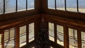 Ein Zimmer mit Holzboden, Deckenventilator, großen Fenstern und einem Weihnachtsbaum.