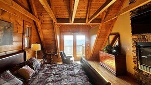 Ein gemütliches Schlafzimmer im Dachgeschoss mit Holzbalkendecke, einem großen Bett, einem Schminktisch und einem Kamin aus Stein.