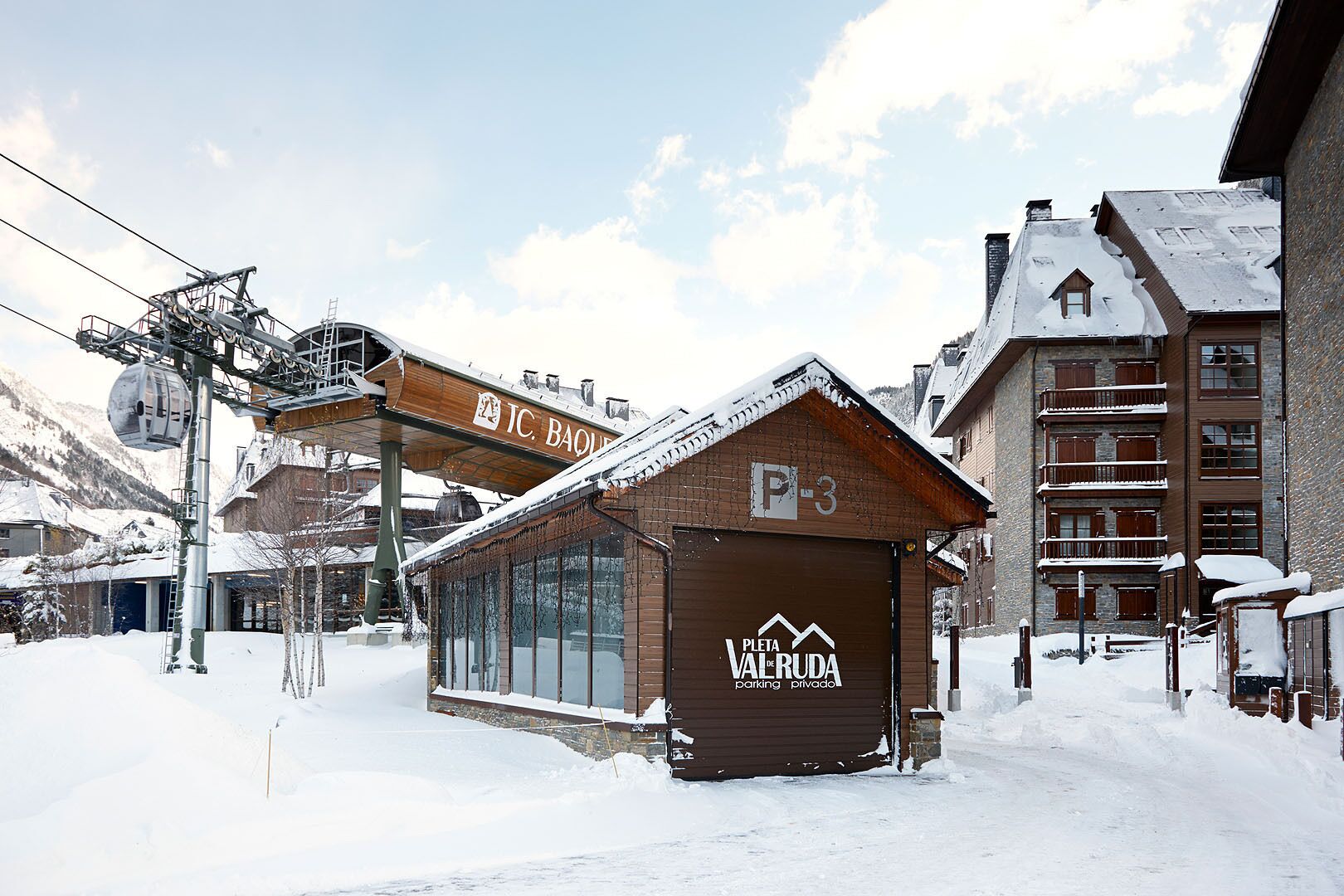 A snow-covered building with a sign reading "Plata de Vairuda parking privado" and a ski lift overhead.