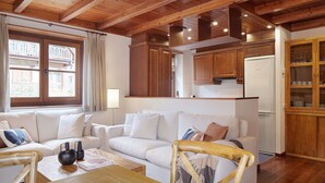 Een gezellige woonkamer met een houten plafond, een witte bank, een houten eettafel en een keuken met houten kasten en een koelkast.