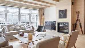 A modern living room with a sofa, chairs, a coffee table, a fireplace, and ski equipment. - Casa Val de Ruda Luxe 71 by FeelFree Rentals (Baqueira)