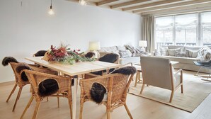 A modern living room with a dining area, featuring wicker furniture, a sofa set, and a large window with curtains. - Casa Val de Ruda Luxe 71 by FeelFree Rentals (Baqueira)