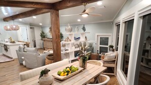 Amplia sala de estar con una mesa de comedor de madera, sillas de mimbre y un arreglo floral central.