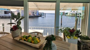 Un comedor con vista al agua, una mesa con frutas y flores, y una silla.