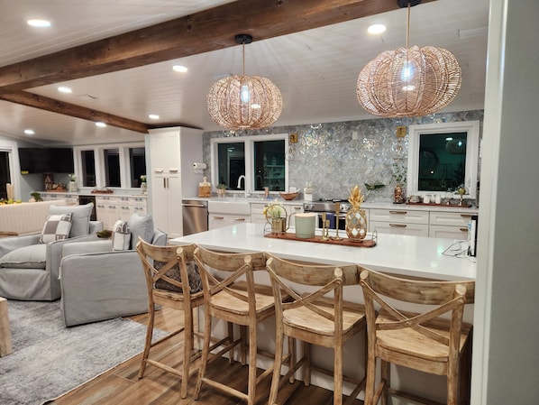 A modern kitchen with a central island, wooden chairs, and pendant lighting.