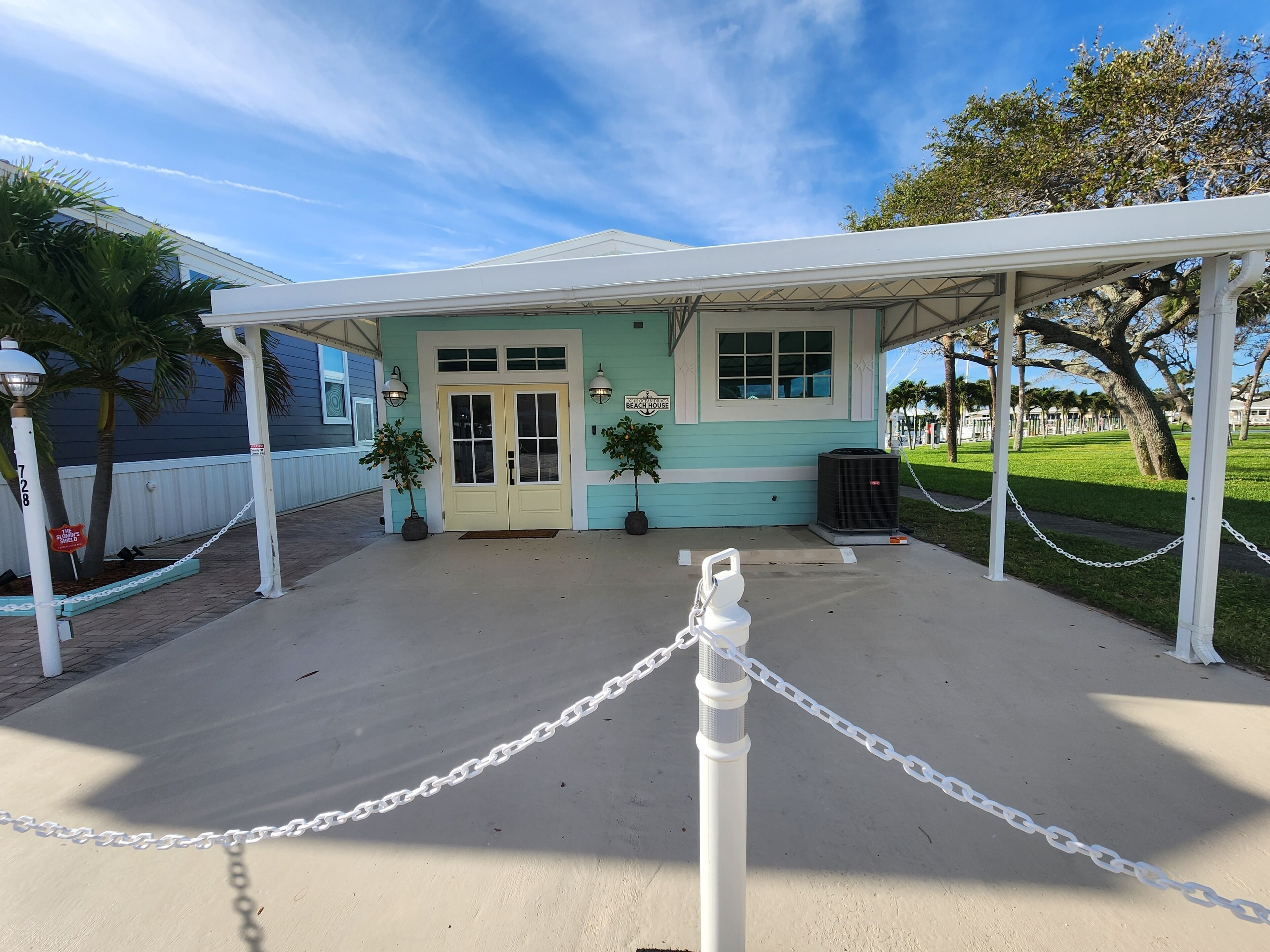 A beach house with a covered porch, two potted plants, and a chain-link fence.