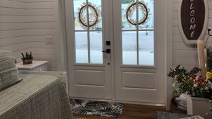 Una habitación con una cama, una mesita con una planta, un cartel de bienvenida y una ventana decorada con un adorno.