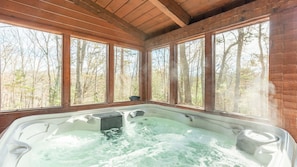 Uma banheira de hidromassagem em uma cabana com grandes janelas e vista para a floresta.