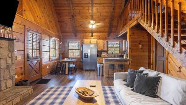Ein gemütliches Blockhaushaus-Interieur mit einer Holztreppe, einem Essbereich, einer Küche und einem Wohnzimmer mit einer Couch und einem Couchtisch.