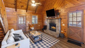 Ein rustikales Blockhaus-Interieur mit Kamin, Holzwänden, einer Couch, einem Couchtisch und einem Fernseher.