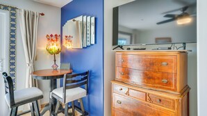 Quarto com parede azul de destaque, cômoda de madeira, mesa redonda com cadeiras e abajur decorativo.