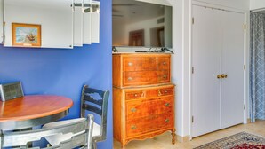 Um quarto com parede azul, cômoda de madeira, porta branca e mesa redonda com cadeiras.