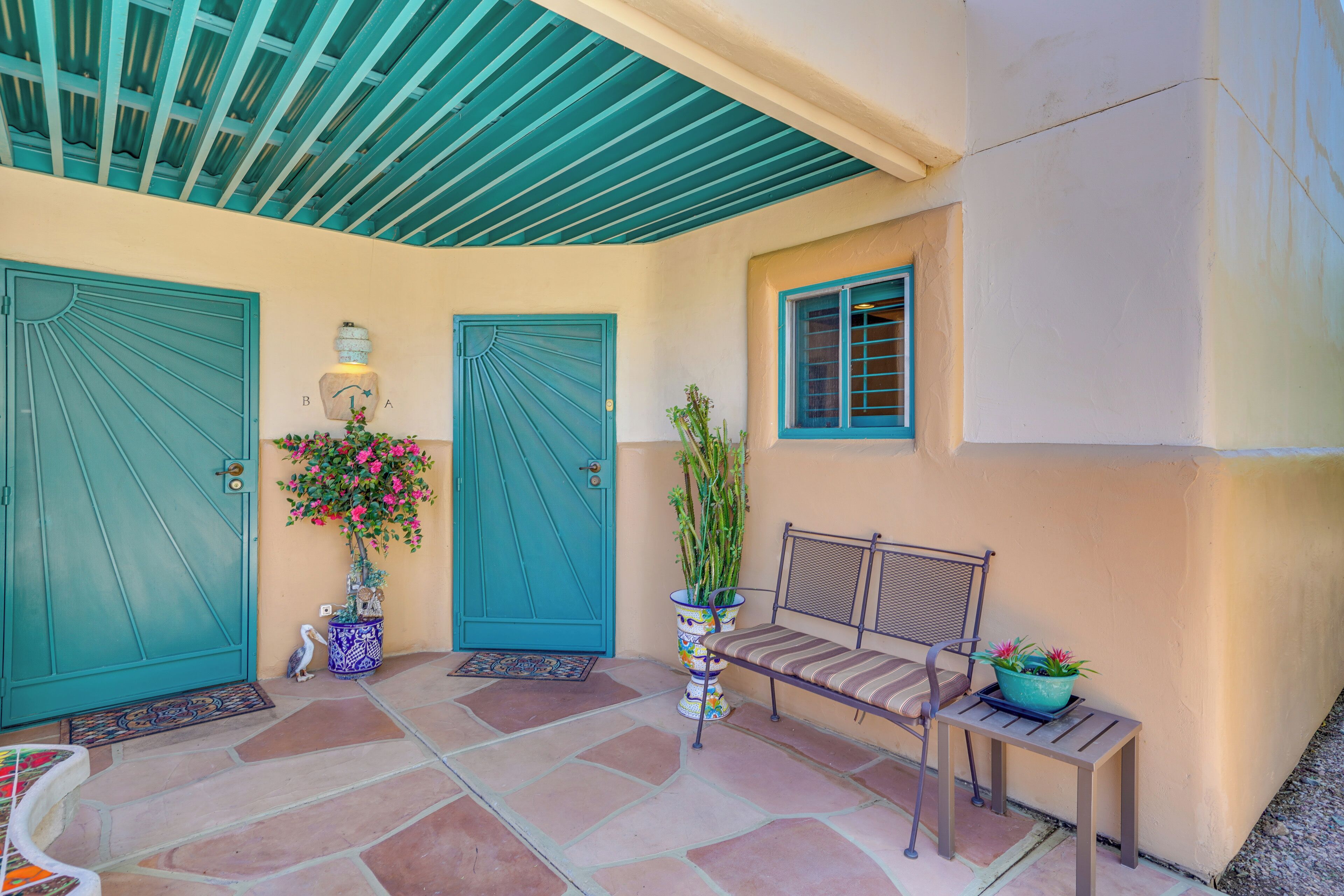 A covered patio with a bench, two doors, and potted plants.