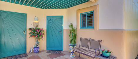 A covered patio with a bench, two doors, and potted plants.