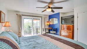 Quarto com cama grande, ventilador de teto, escrivaninha com cadeiras e cómoda.