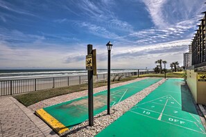 A green shuffleboard court with caution signs, a lamp post, and a view of the ocean. - Oceanfront Getaway w/ Beach & Resort Access! (Daytona Beach Shores)