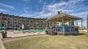 Een hotel met een zwembad, terras en een gazebopaviljoen met rieten dak.
