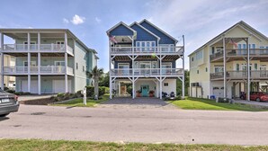 A two-story beachfront building with balconies, a covered front porch, and a flag. - Charming Surf City Home w/ Elevator: Walk to Beach (Holly Ridge)