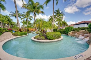 A swimming pool with a waterfall feature, surrounded by palm trees and lush greenery. - Luxe Naples Bay Resort Condo: Near Fifth Ave! (Naples)