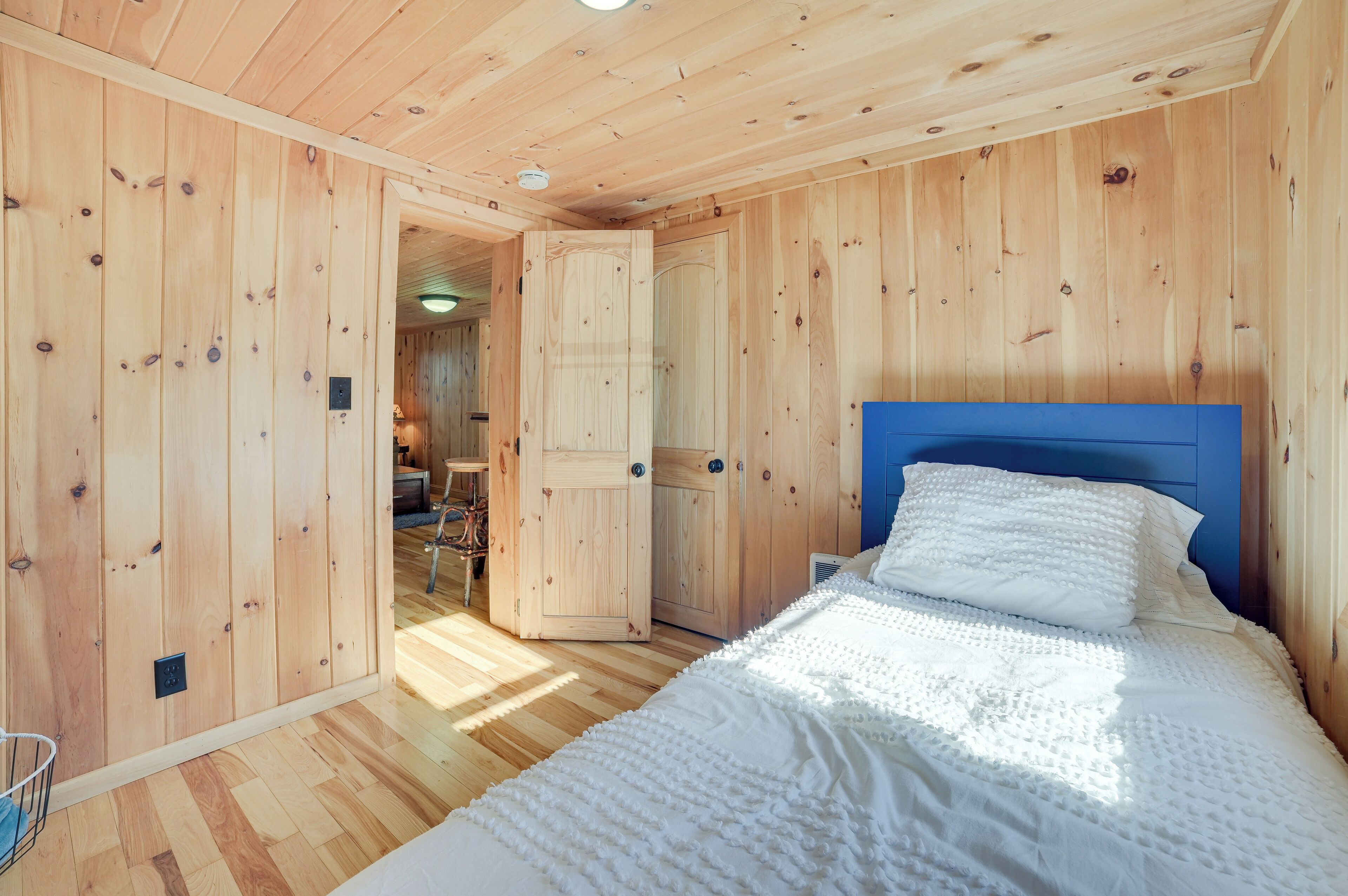 A wooden-paneled room with a bed, a door, and a small table.