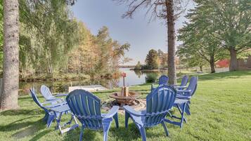 A lakeside outdoor seating area with Adirondack chairs and a fire pit.