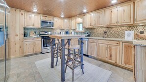 Uma cozinha com armários de madeira, uma ilha central com banquetas, micro-ondas e painel de azulejos.