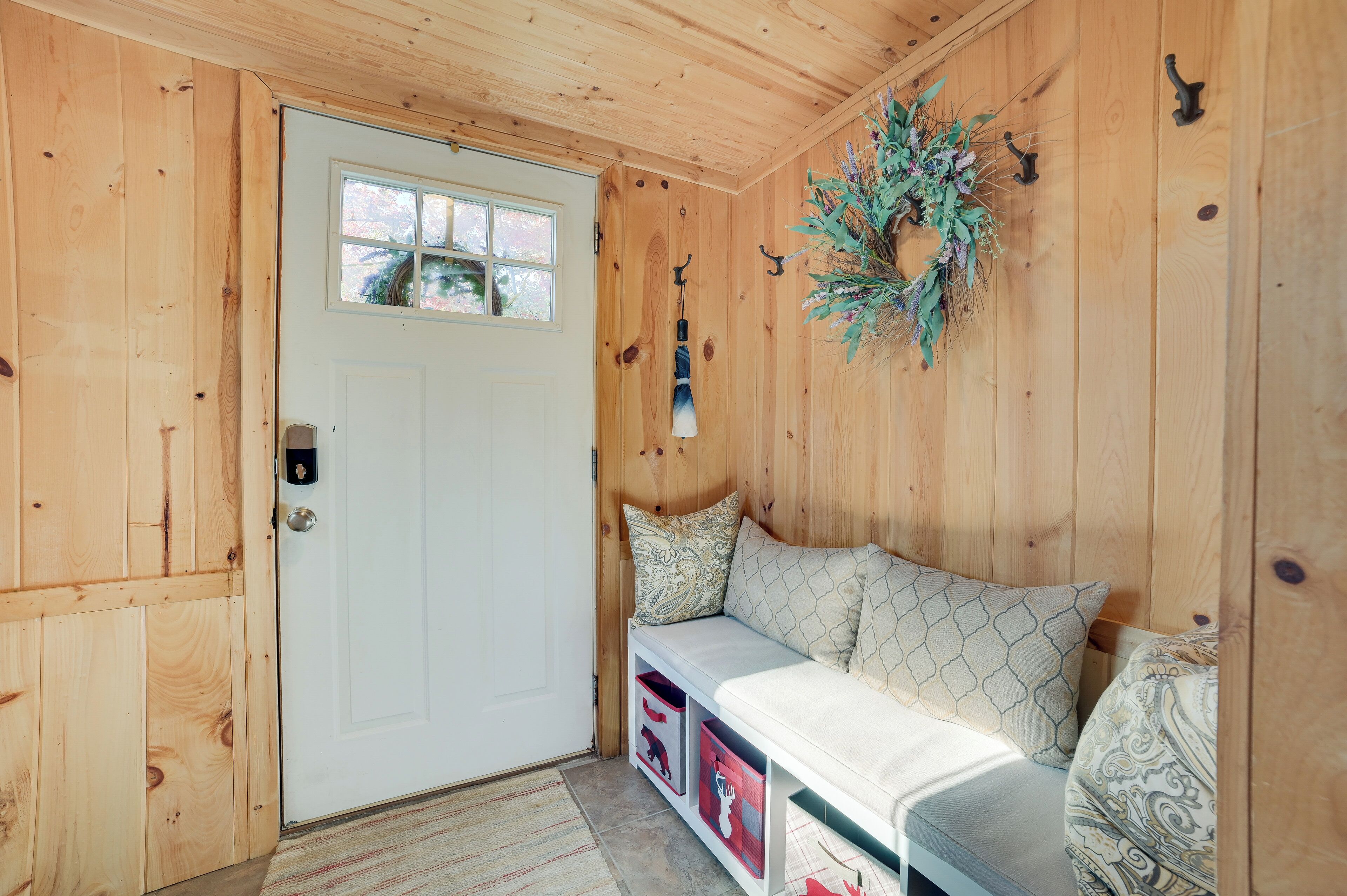 Un intérieur en bois avec une porte blanche, un banc agrémenté de coussins à motifs et une guirlande accrochée au mur.
