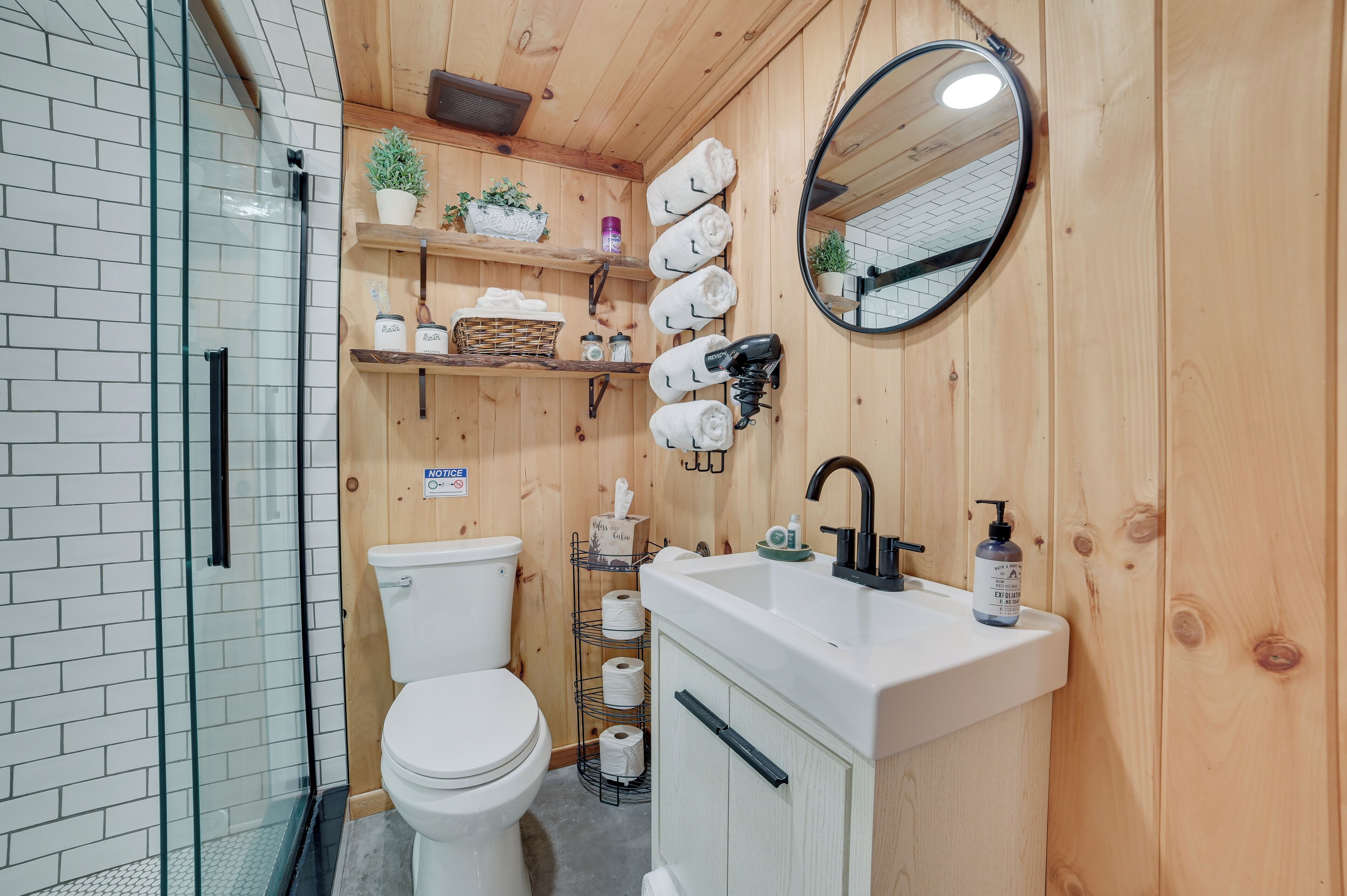 Ein Badezimmer mit einer weißen Toilette, einem Waschbecken inklusive Spiegel und Regalen mit Handtüchern und Pflegeprodukten.
