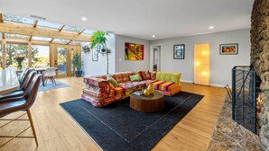 A spacious living area with a wooden floor, a colorful sofa, a round coffee table, and a stone fireplace.