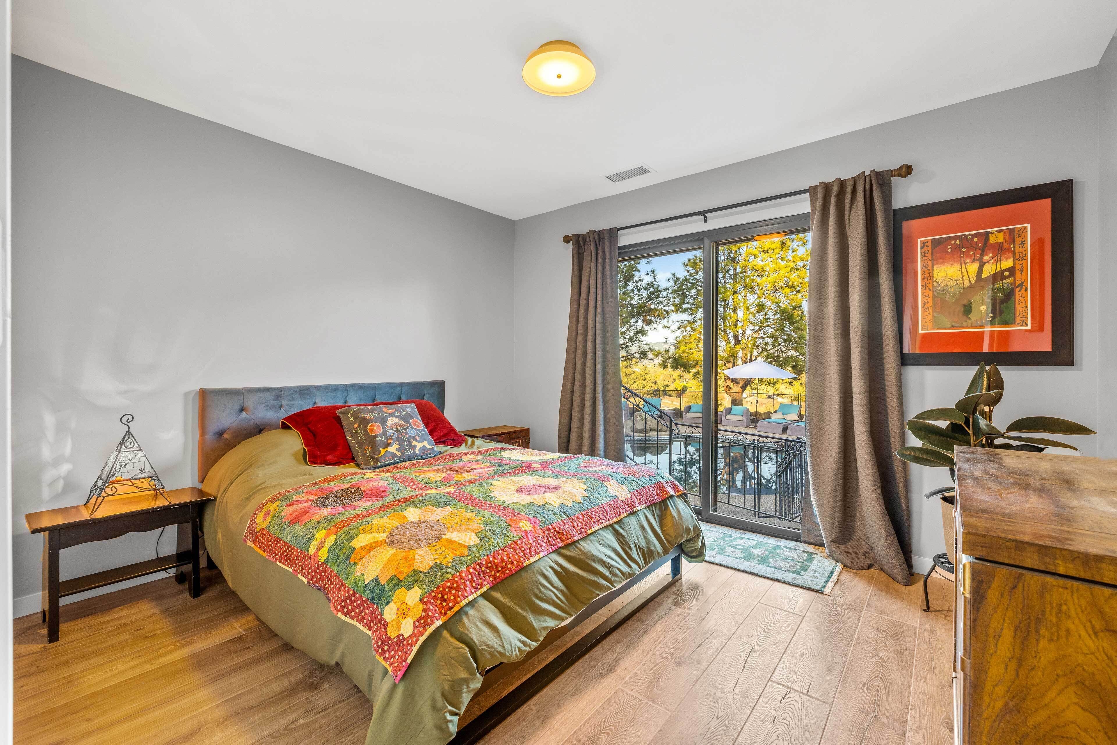 A bedroom with a large bed, a nightstand, a dresser, and a window with curtains.