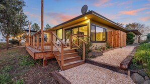 A modern house with a wooden deck, a staircase leading to a glass door, and a gravel pathway.