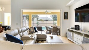 A spacious living room with a large sofa, a coffee table, and a TV. There is a balcony with a pool and palm trees visible through the glass doors. - Florida Vacation Rental w/ Private Pool & Lanai (North Port)